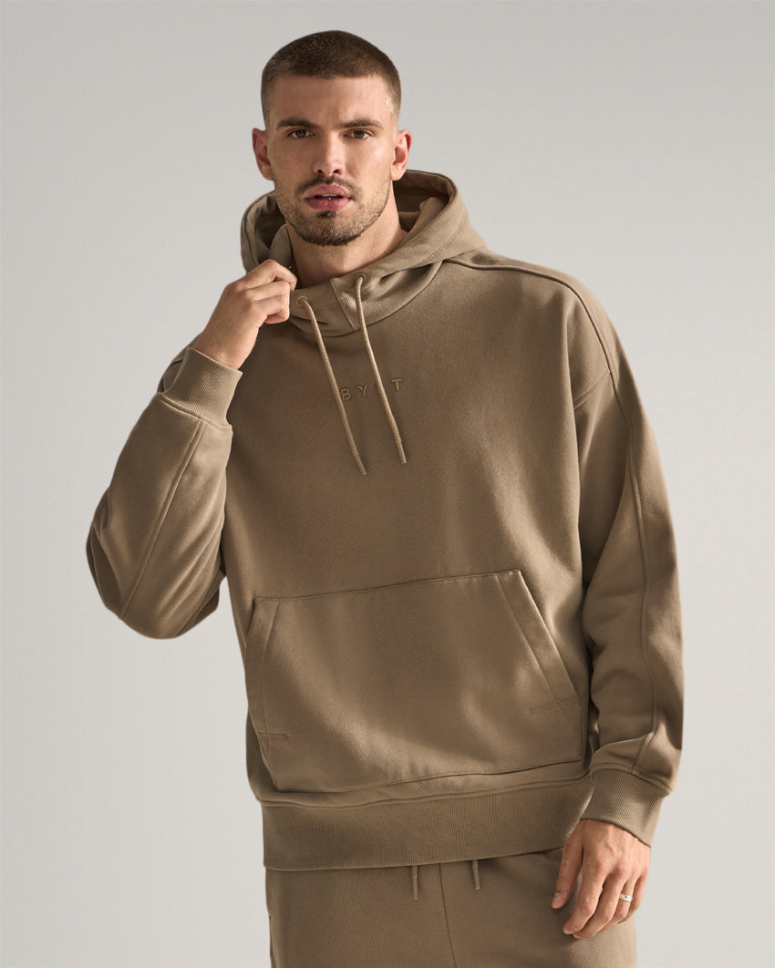 Taupe | Front view of the Heavyweight Fleece Hoodie with hand on the hood and front kangaroo pocket